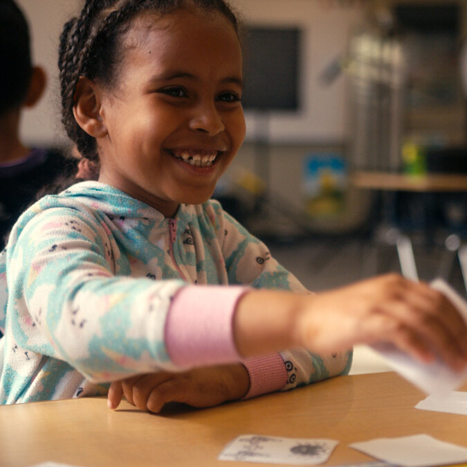 Young female student smiling while playing with cards.