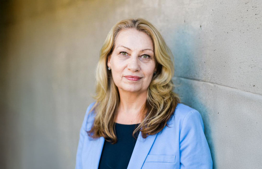 Woman in blue blazer standing against concrete wall.